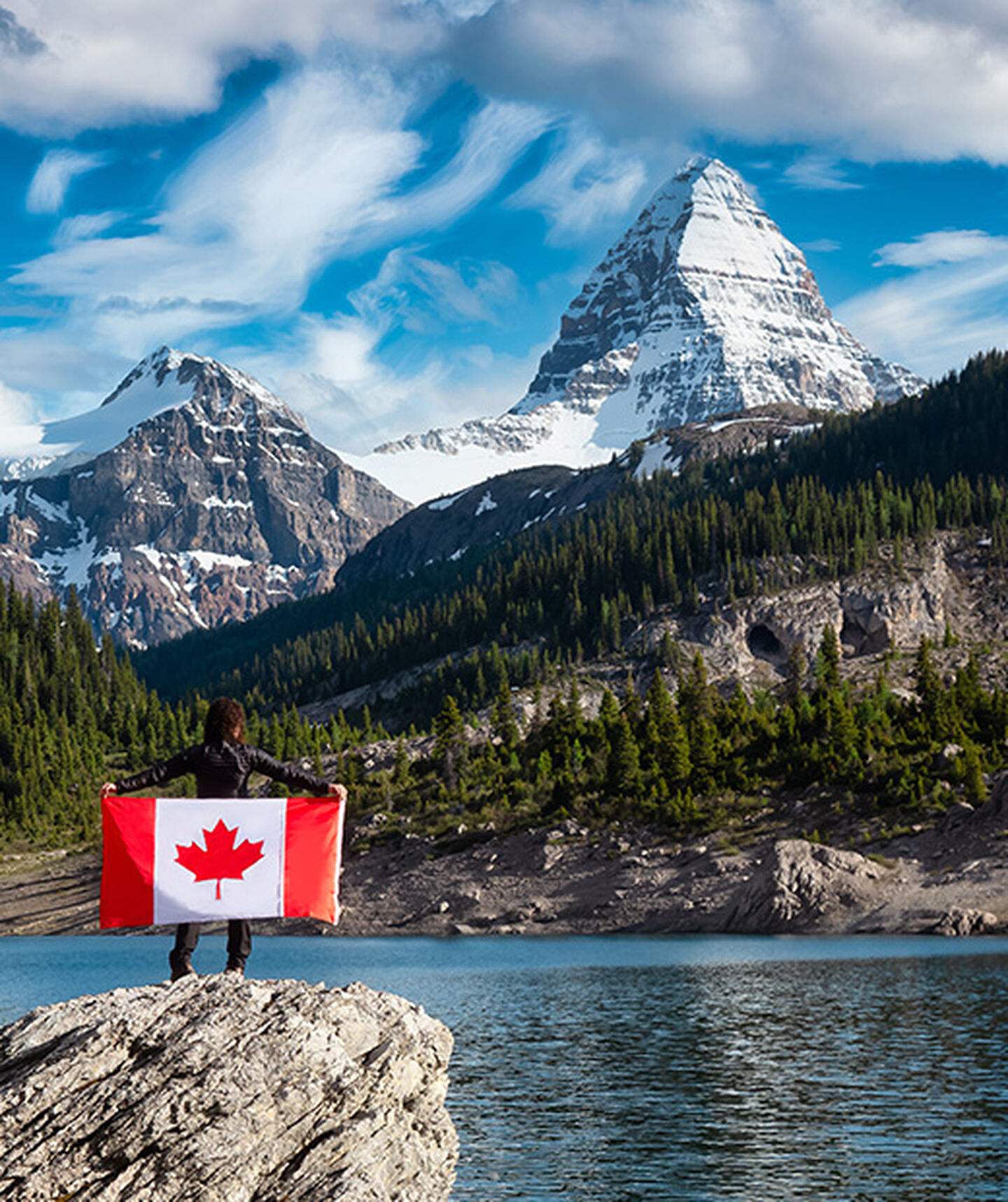 a person holds a canadian flag while looking at the mountains